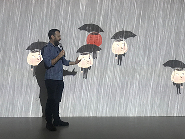 A man standing in front of an digital artwork and talks into a microphone